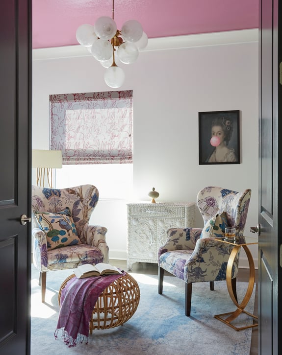 A private sitting room with floral wingback chairs, a chest covered in sea shells, and a painting of Marie Antoinette with pink bubblegum, bunny window treatment, and bubble chandelier - interior design by Jasmin Reese Interiors, Chicago, USA. 