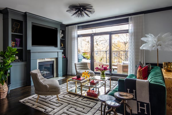 An eclectic media room with a large emerald green sofa, tweed clutch chairs, and a glass and brass, multi-level coffee table on a cream and black patterned rug - living room design by Jasmin Reese Interiors, Chicago, USA. 