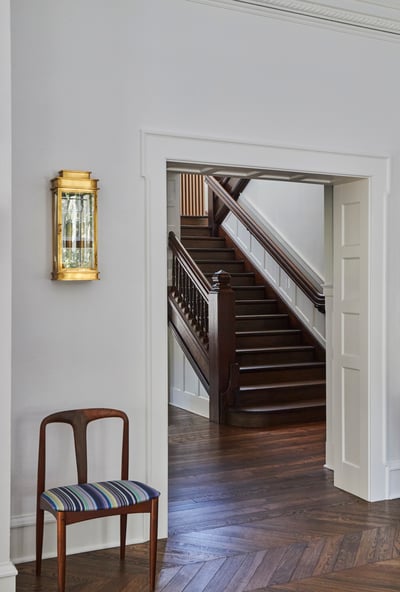 A modernist chair beside a large archway leading to an antique, dark wooden staircase - living room design by Jasmin Reese Interiors, Chicago, USA. 
