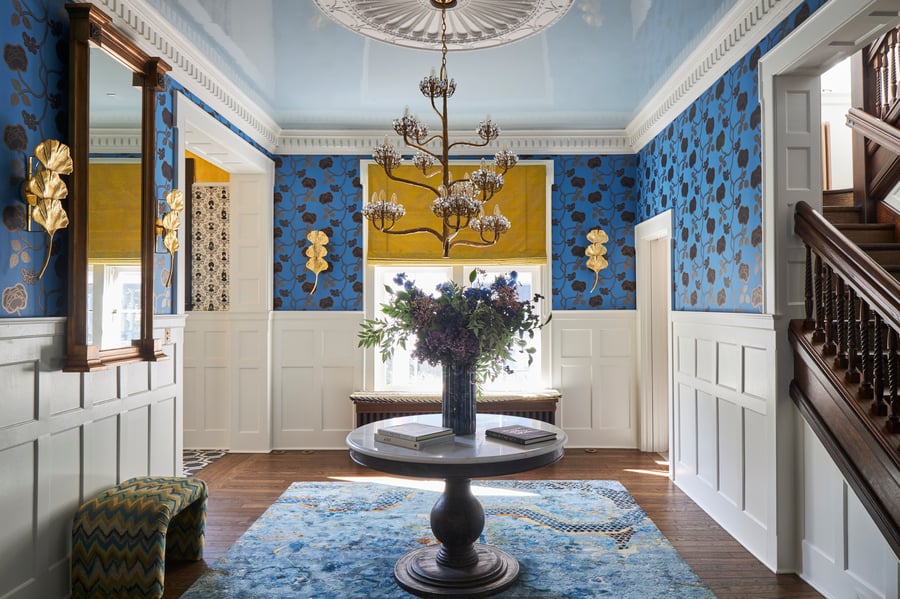 An antique marble and wood table in a small blue and gold living room space beside an antique wooden staircase - designed by Jasmin Reese Interiors, Chicago, USA. 