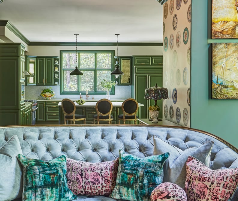 A bright kitchen with green and cream cabinetry and accents seen over the back of a  Victorian sofa upholstered in light blue - living room design by Jasmin Reese Interiors, Chicago, USA. 