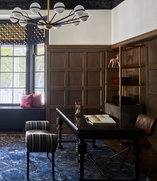 A large study with a window seat designed by Jasmin Reese: dark wood furniture, blue rug, and hardwood floors, Chicago, USA.