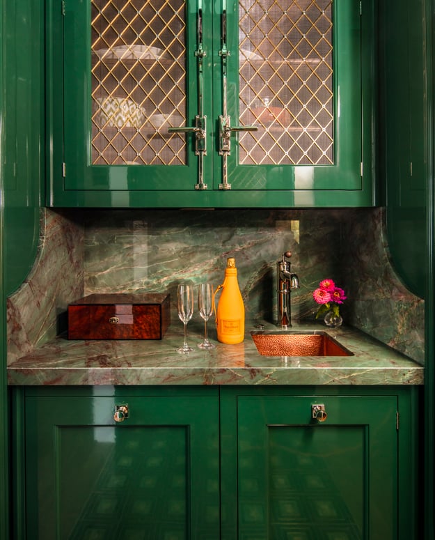A wet bar with green and brown marble and green cabinets designed by Jasmin Reese, Chicago. 