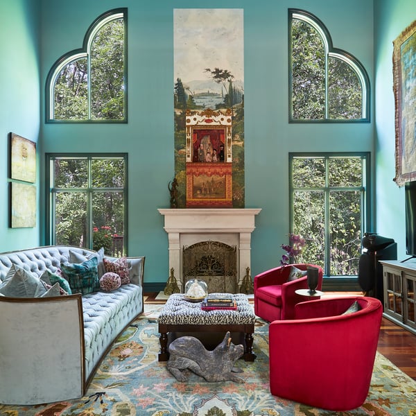 A large living room with high ceilings with ornate windows that look out over trees outside - a Victorian sofa is upholstered in light blue to match the muted green tones - living room design by Jasmin Reese Interiors, Chicago, USA. 