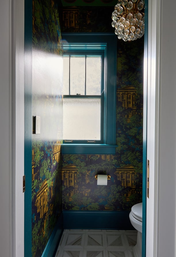 A view from a hallway of a small bathroom designed by Jasmin Reese, Chicago with bold gold, green, and turquoise wallpaper. 
