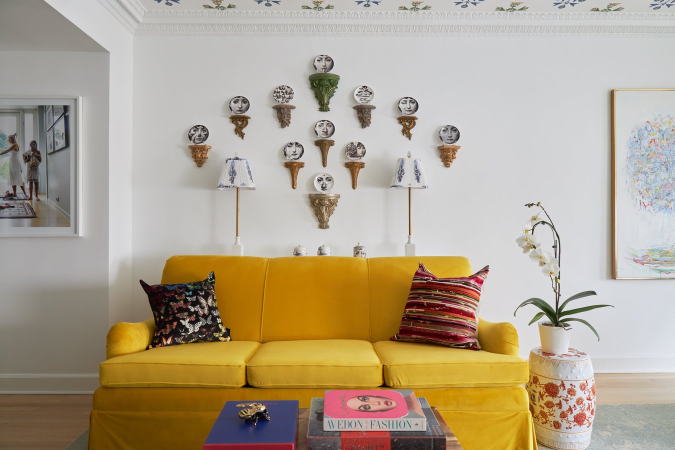 A bright yellow sofa with an ornate display of small plates with a person's face wearing different expressions - living room design by Jasmin Reese Interiors, Chicago, USA. 