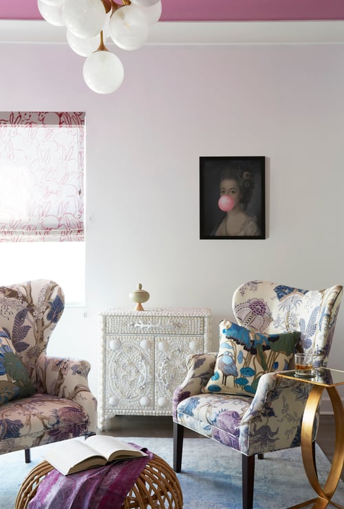 A private sitting room with floral wingback chairs, a chest covered in sea shells, and a painting of Marie Antoinette with pink bubblegum, bunny window treatment - interior design by Jasmin Reese Interiors, Chicago, USA. 