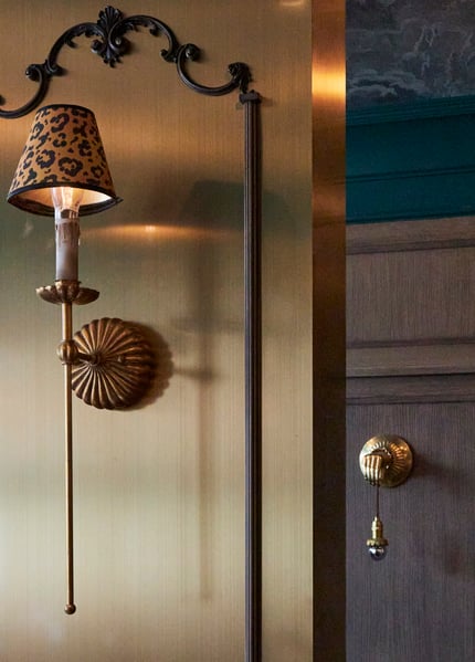 A wall sconce with a leopard print lamp shade on a brass plated wall in a bar area of a home - interior design by Jasmin Reese Interiors, Chicago, USA. 