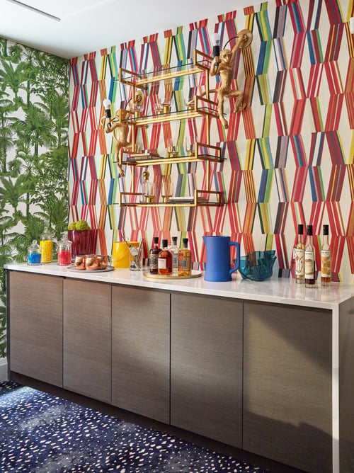 Whimsical bar by Jasmin Reese: wood, enamel cabinets, brass shelf, monkey lights, geometric wallpaper, on blue star carpet, Chicago.