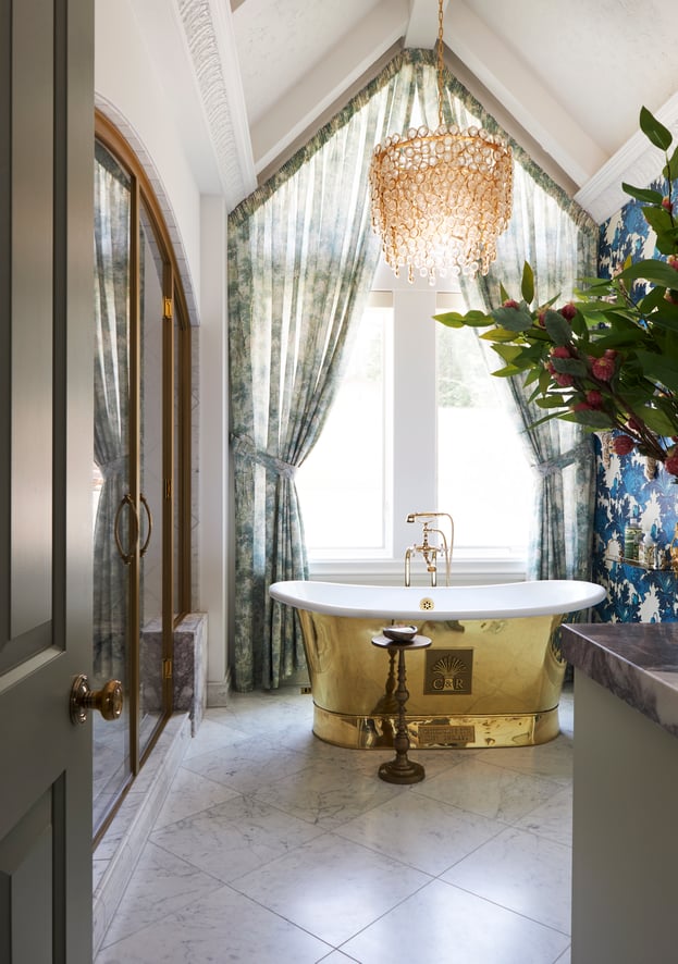 A large marble bathroom with a brass bathtub and chandelier designed by Jasmin Reese, Chicago. 