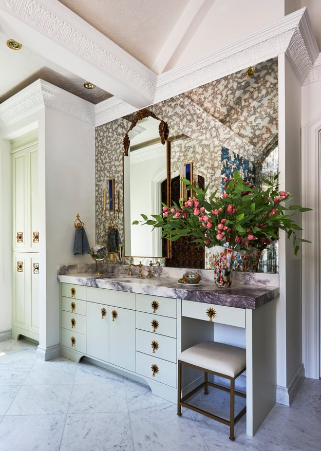 A marble top vanity with foil wallpaper and unique brass fixtures in a bathroom designed by Jasmin Reese, Chicago. 