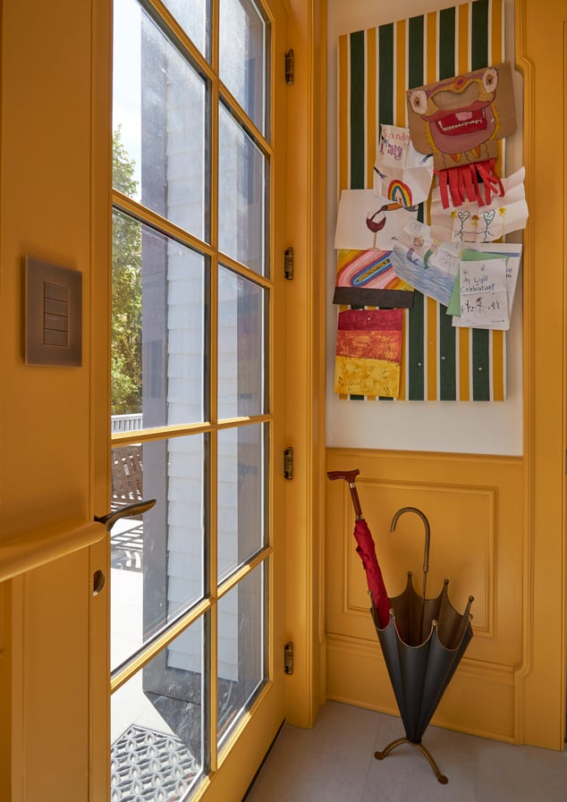 A bright yellow mudroom with an umbrella stand & kids' art on the wall - interior design by Jasmin Reese Interiors, Chicago, USA. 