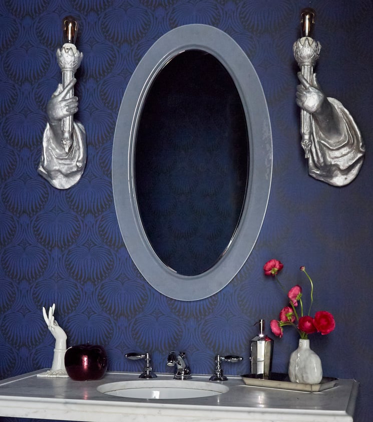 A small vanity sink in a bathroom designed by Jasmin Reese with unique hand-held sconces around the mirror. 