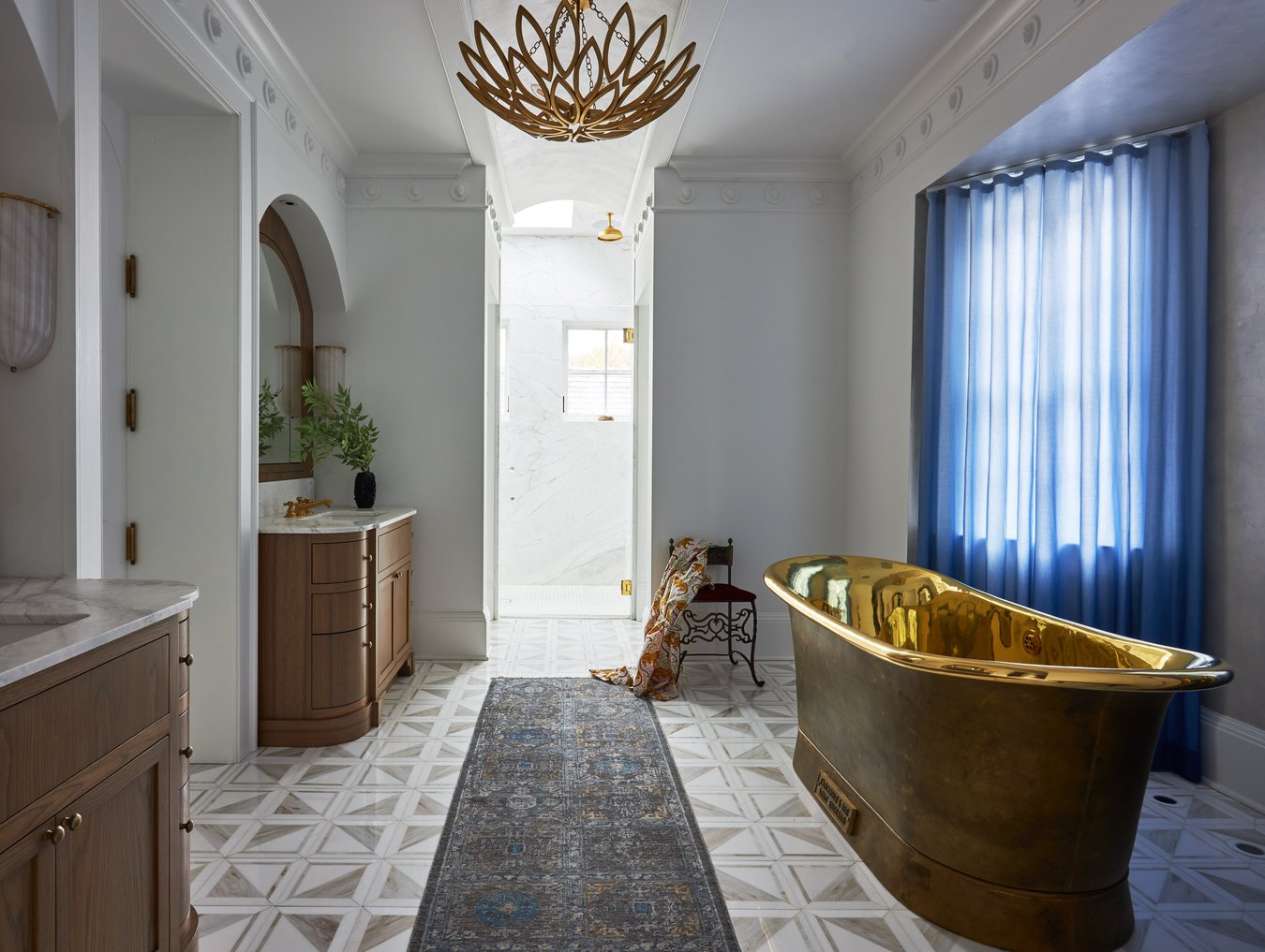 A beautiful bathroom designed by Jasmin Reese with a large copper bathtub, a copper chandelier, a small iron chair, and a long gray rug on geometric flooring, in Chicago, USA. 