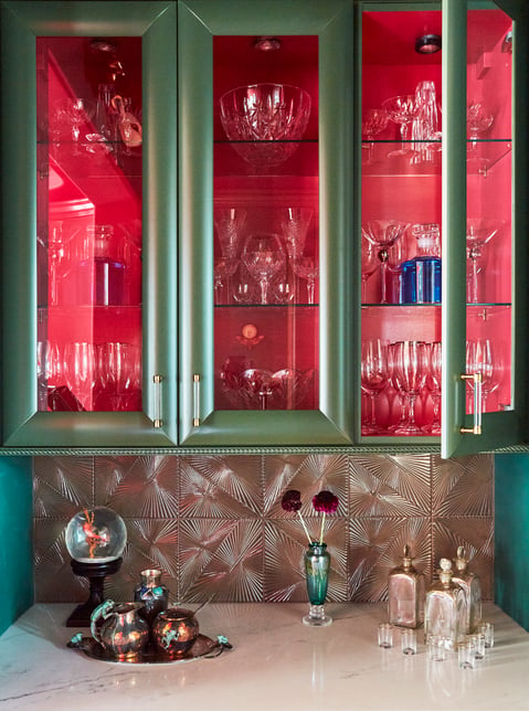 A marble dry bar with a glass cabinet for crystal glassware designed in red, green, and silver by Jasmin Reese, Chicago. 