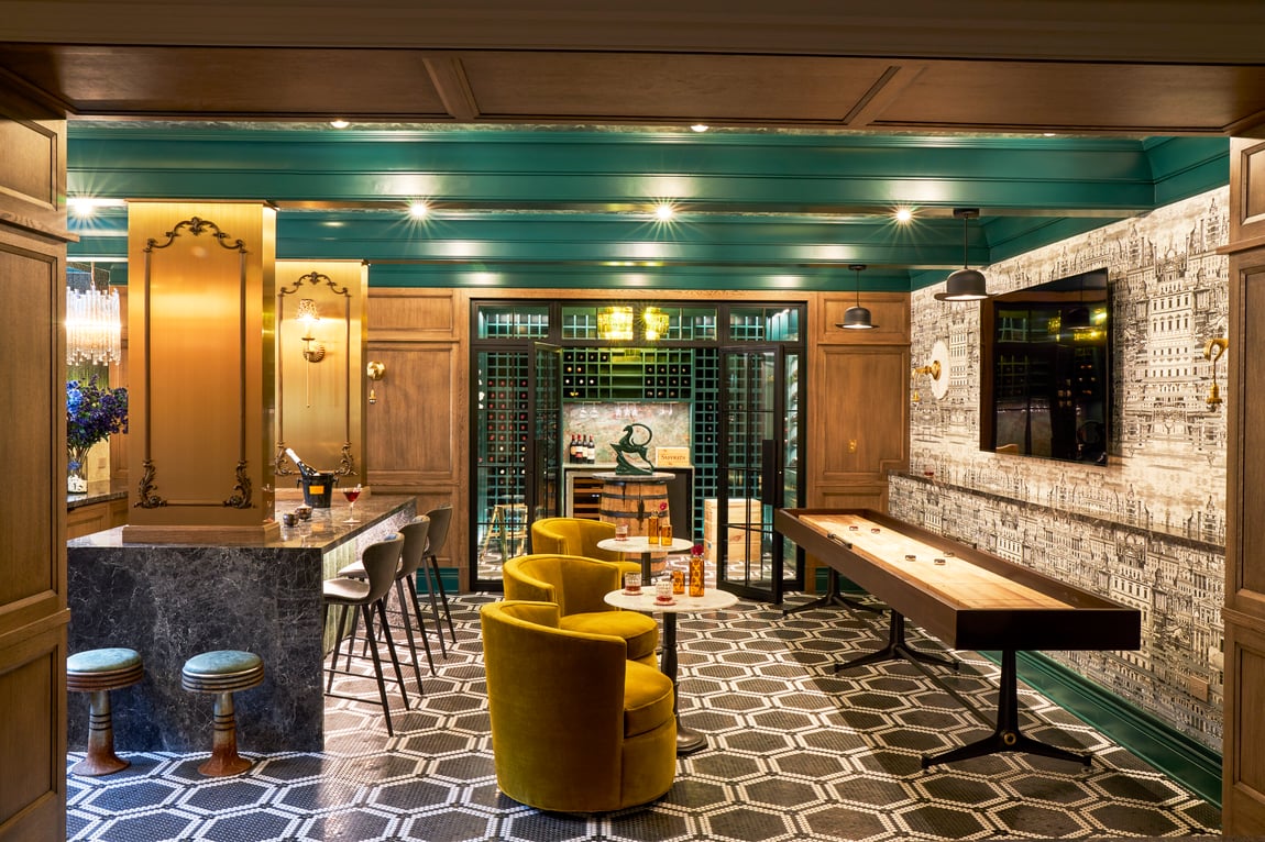 A side view of a bar area highlighting a shuffleboard table, forest green ceilings, bowler hat lights, and a wine and cigar humidifier - interior design by Jasmin Reese Interiors, Chicago, USA. 