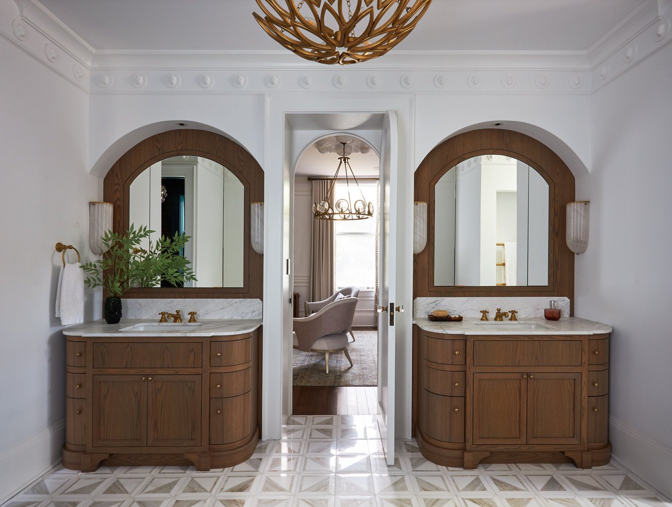 Double vanity sinks with rounded, oak cabinets and marble countertops in a bathroom designed by Jasmin Reese, Chicago.
