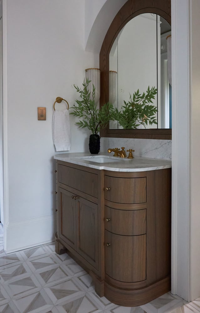 A vanity sink with rounded, oak cabinets and marble countertop in a bathroom designed by Jasmin Reese, Chicago.