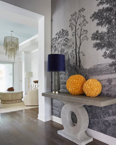 A hallway with a marble table with glass lamps with bright blue lampshades and wallpaper featuring pastoral trees in gray - living room design by Jasmin Reese Interiors, Chicago, USA. 