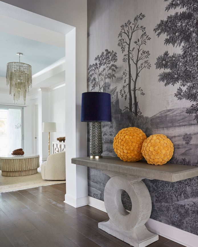 A hallway with a marble table with glass lamps with bright blue lampshades and wallpaper featuring pastoral trees in gray - living room design by Jasmin Reese Interiors, Chicago, USA. 