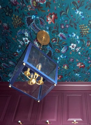 A blue metal and glass cube chandelier with brass fixtures against a turquoise and floral wallpapered ceiling and metallic magenta cabinetry on the walls - interior design by Jasmin Reese Interiors, Chicago, USA. 