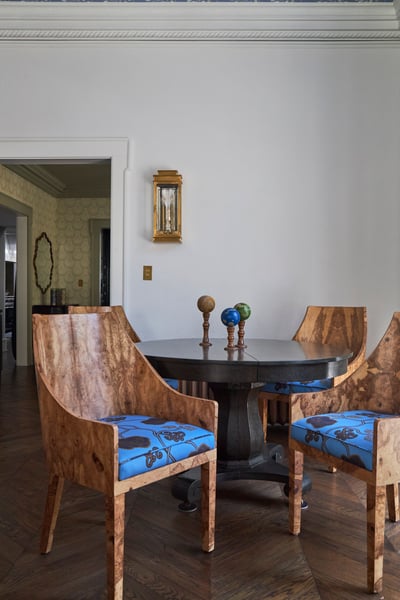Four wooden chairs with natural patterns and bright blue cushions around a black marble table in a white room - living room designed by Jasmin Reese Interiors, Chicago, USA. 
