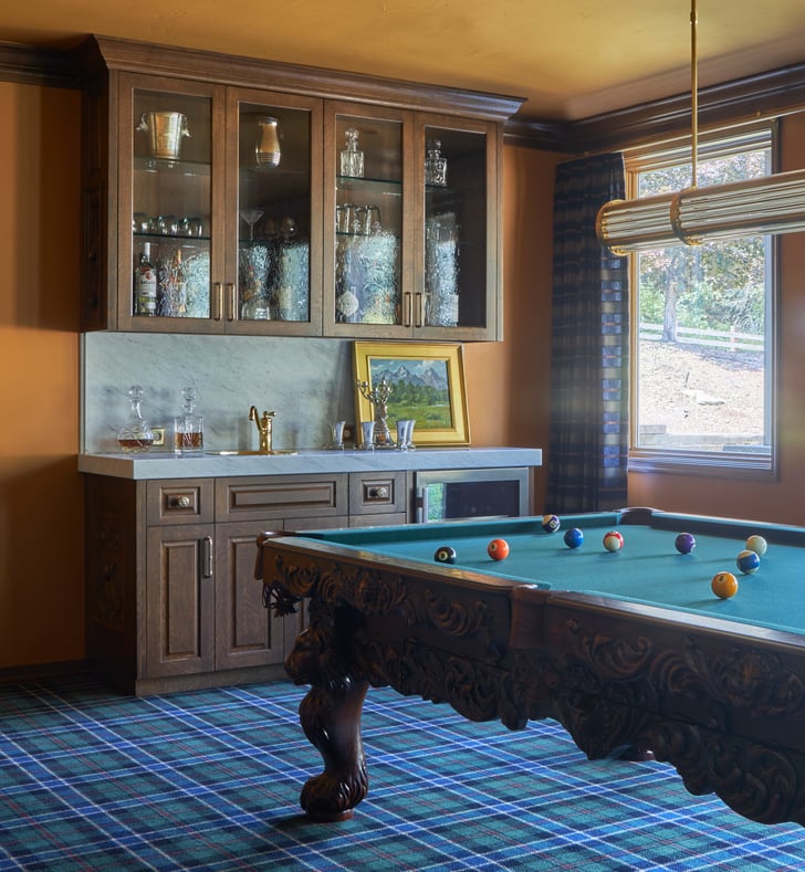 A wet bar with marble counters and rustic wood and glass cabinetry by a pool table in a home - interior design by Jasmin Reese Interiors, Chicago, USA. 