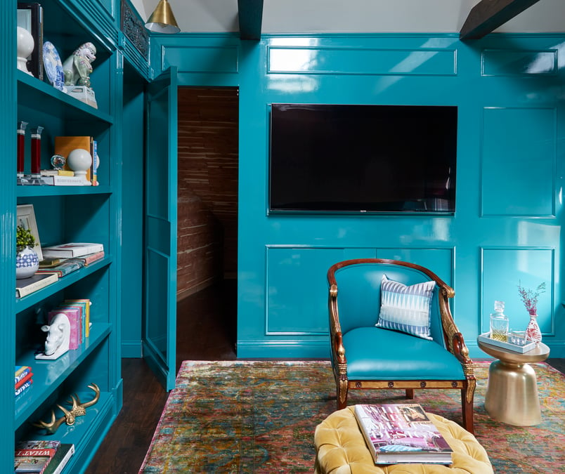 A detail of an open secret door in a living room painted in turquoise paint with a slick, shiny finish with a turquoise leather armchair and gold pin cushion ottomans - living room design by Jasmin Reese Interiors, Chicago, USA. 