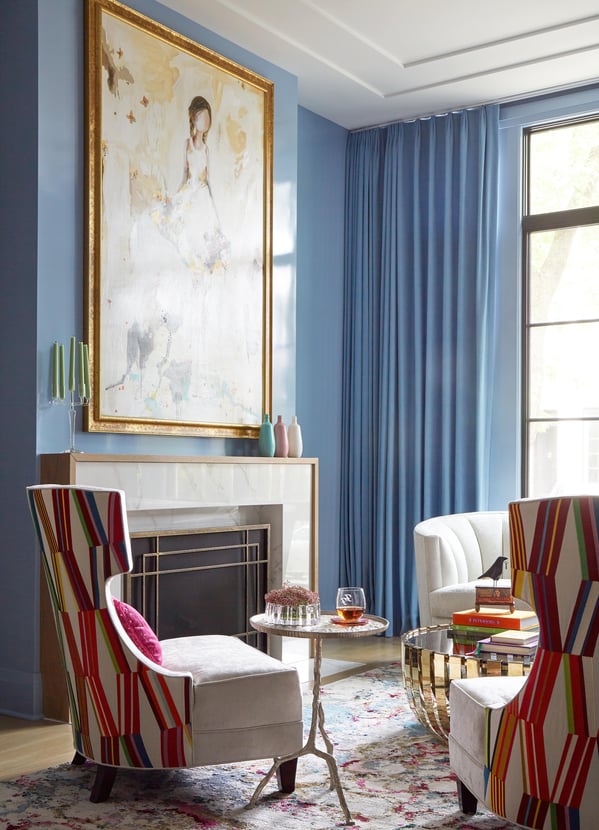 Bold, colorful geometric patterns on the backs of low wing-back chairs highlight a light blue room with a modernist fireplace, large portrait art, and metal and glass coffee table - living room design by Jasmin Reese Interiors, Chicago, USA. 
