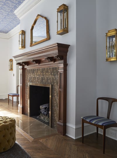 A hearth with an antique wooden mantle with modern swirl accents around the fireplace. Two modernist chairs are placed on either side - living room design by Jasmin Reese Interiors, Chicago, USA. 