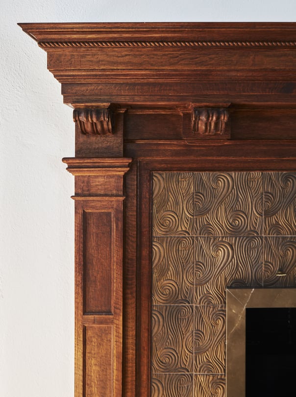 A detailed view of a mantlepiece styled in antique carved rough-finish cherry with an inset metal carving of spirals - living room design by Jasmin Reese Interiors, Chicago, USA. 