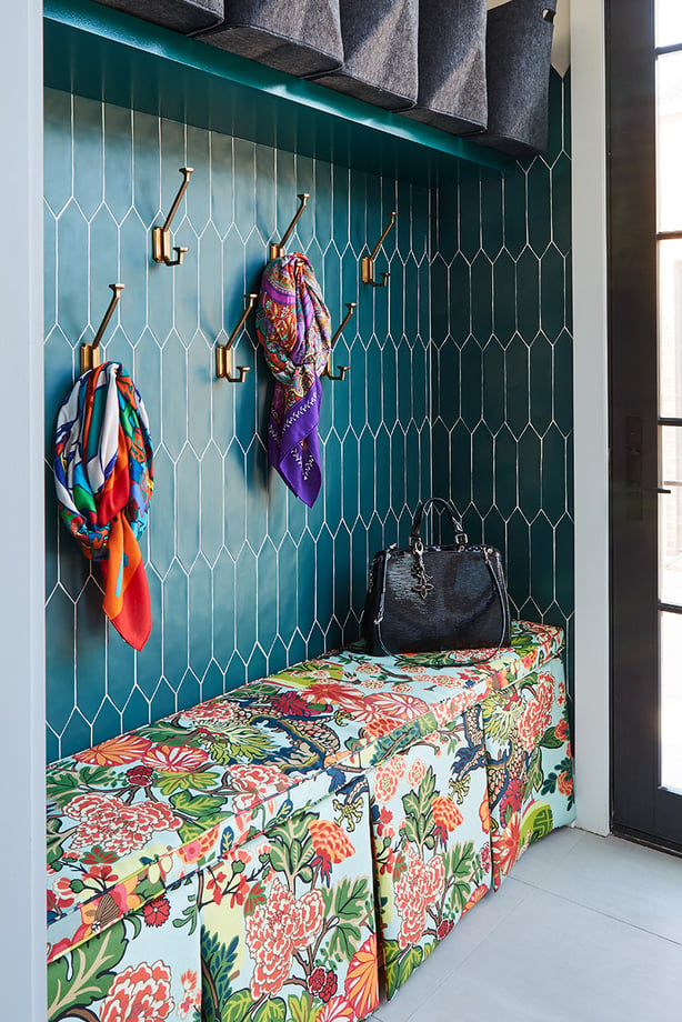 A mudroom with teal tile, brass hooks with colorful scarves hanging from them, and a floral upholstered bench - interior design by Jasmin Reese Interiors, Chicago, USA. 