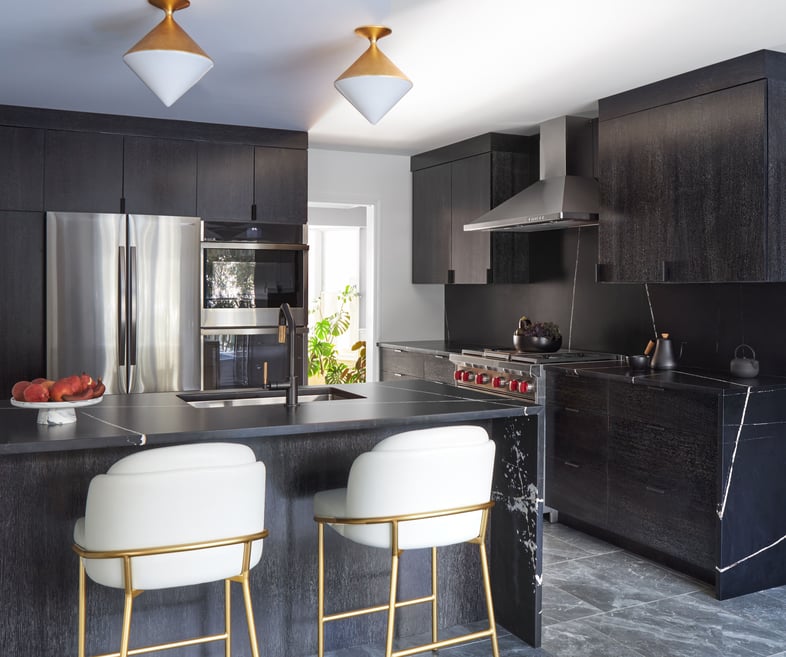 A minimalist black kitchen designed by Jasmin Reese with stainless appliances and white bar stools, Chicago. 