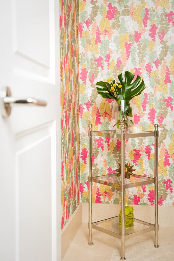 A brass & glass multi-level table in a bathroom with bright neon wallpaper designed by Jasmin Reese, Chicago. 