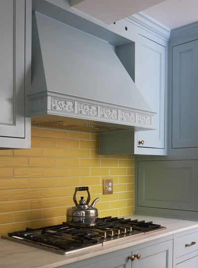 Gold subway tile backsplash behind a stove in a powder blue kitchen designed by Jasmin Reese, Chicago. 