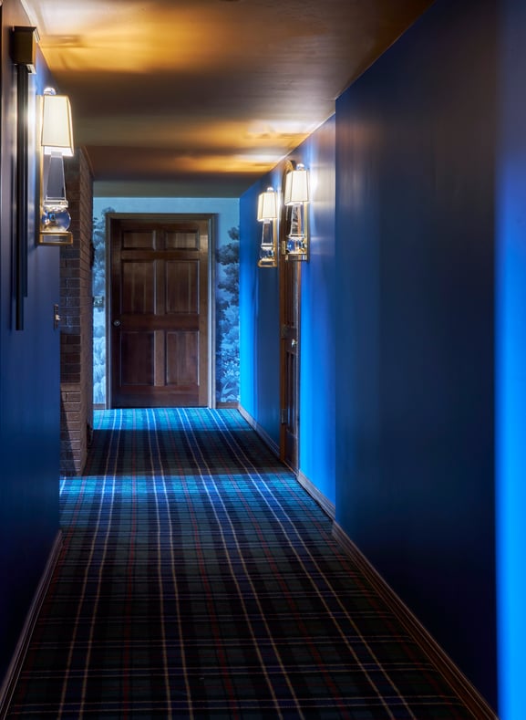 A long hallway with blue, green, and red flannel carpeting, bright blue walls, gold ceilings, and heavy wooden doors - interior design by Jasmin Reese Interiors, Chicago, USA. 