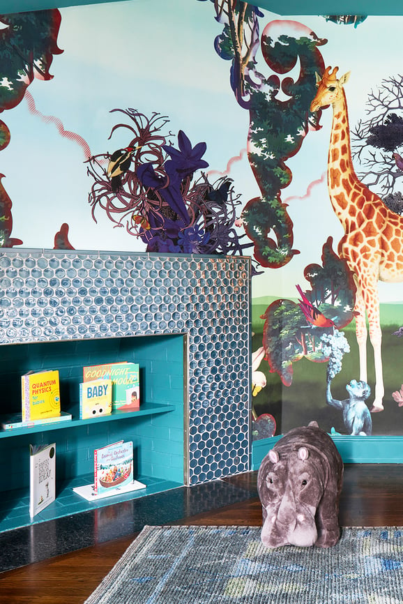 A closeup of a bookshelf repurposed from an old fireplace in a child's playroom with a stuffed giraffe and hippo next to wallpaper with giraffes, monkeys, trees, tropical flowers, and woodpeckers - interior design by Jasmin Reese Interiors, Chicago, USA. 