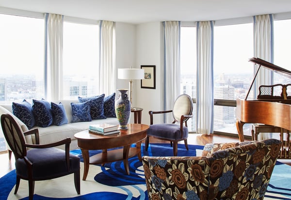 A blue, brown, and white living room with an antique baby grand piano in a room surrounded by floor-to-ceiling windows with blue and white drapes - living room design by Jasmin Reese Interiors, Chicago, USA. 