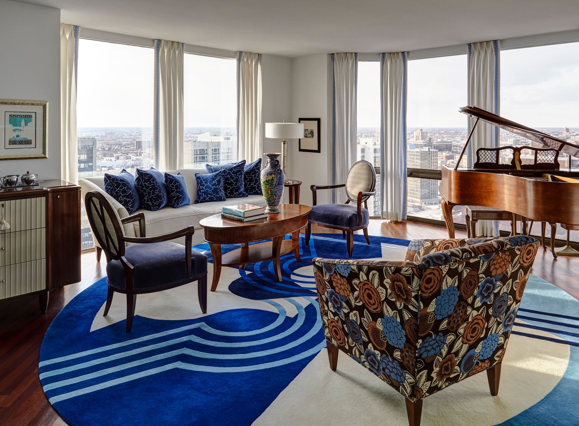 A view of a blue, brown, and white living room with a large bright blue spiral-designed rug surrounded with floor-to-ceiling windows with blue and white drapes - living room design by Jasmin Reese Interiors, Chicago, USA.