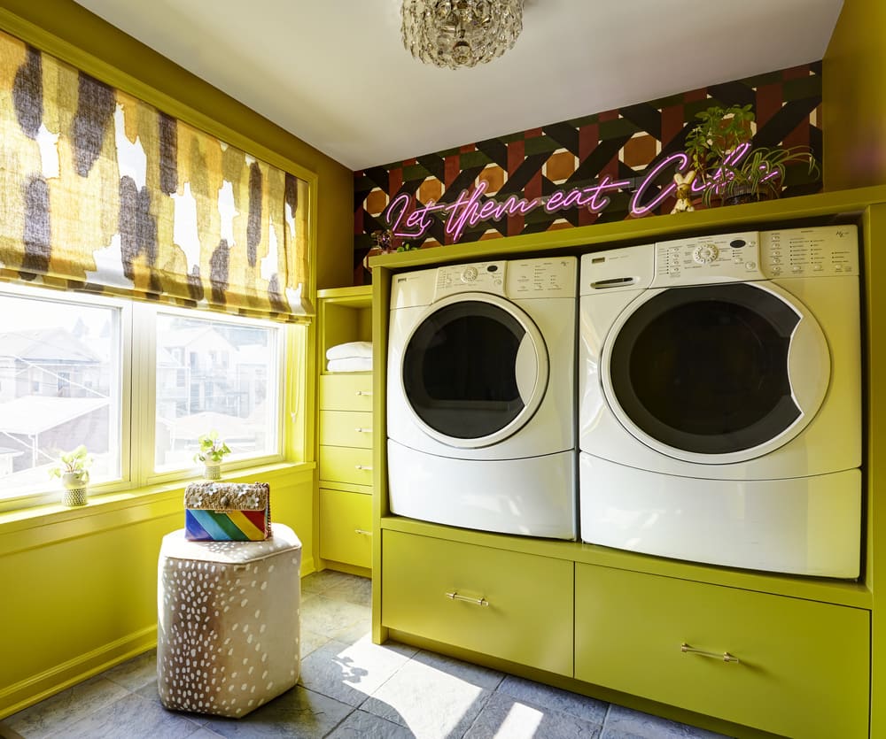 A laundry room with a side-by-side modern washer and dryer with chartreuse cabinetry and window treatment with 