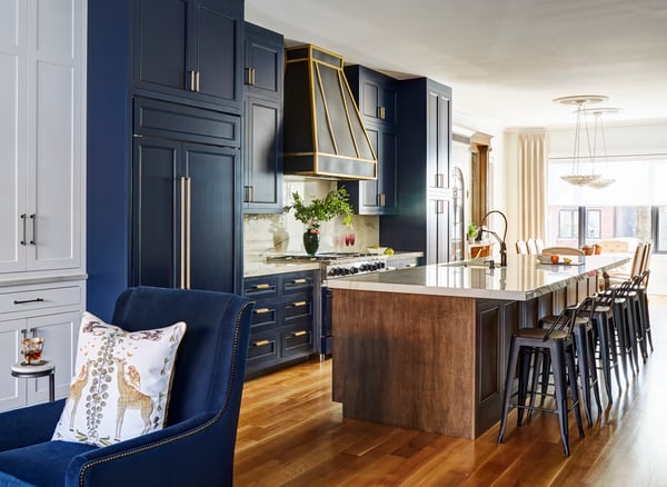 A view from a living room of an open galley kitchen with bright blue cabinetry and a long bar with low-back barstools - living room design by Jasmin Reese Interiors, Chicago, USA. 