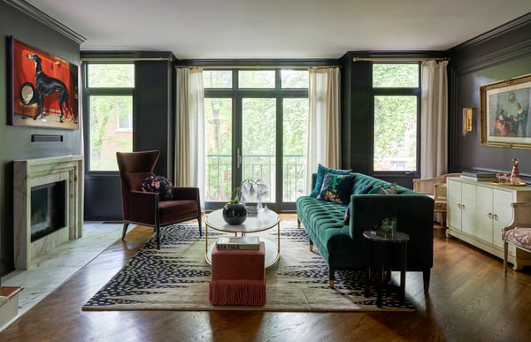 A warm living room with an emerald green sofa, brown velvet sofa, and an orange square ottoman with a large painting of a greyhound against an orange background above the fireplace - living room design by Jasmin Reese Interiors, Chicago, USA. 
