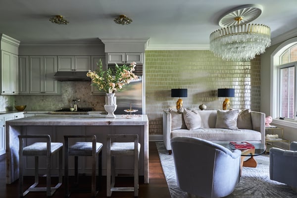 A small living room with a cream sofa and grey circular armchairs against green and gold foil wallpaper beside a small kitchen - living room design by Jasmin Reese Interiors, Chicago, USA. 