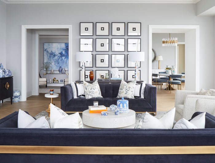 A living room with a long dark grey sofa with white armchairs and a table with glass lamps in front of a collection of sixteen framed pictures of a square with a circle inside - living room design by Jasmin Reese Interiors, Chicago, USA. 