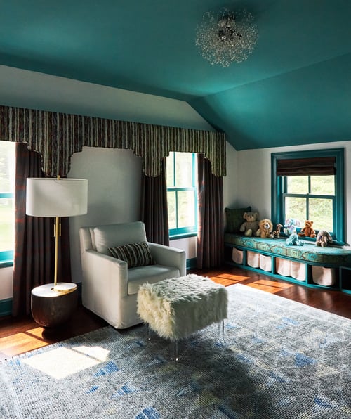 A child's nursery with a soft cream rocking chair with an animal skin ottoman and modern lamp next to a window seat with stuffed animals - interior design by Jasmin Reese Interiors, Chicago, USA.
