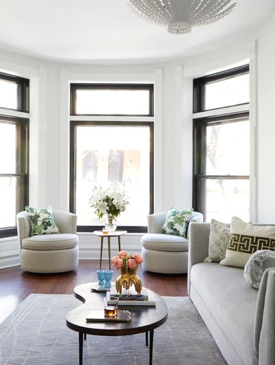 A bright circular room with two white circular armchairs with throw pillows with houseplant designs at the end of a living room with a long grey sofa and a kidney-shaped coffee table - living room design by Jasmin Reese Interiors, Chicago, USA.