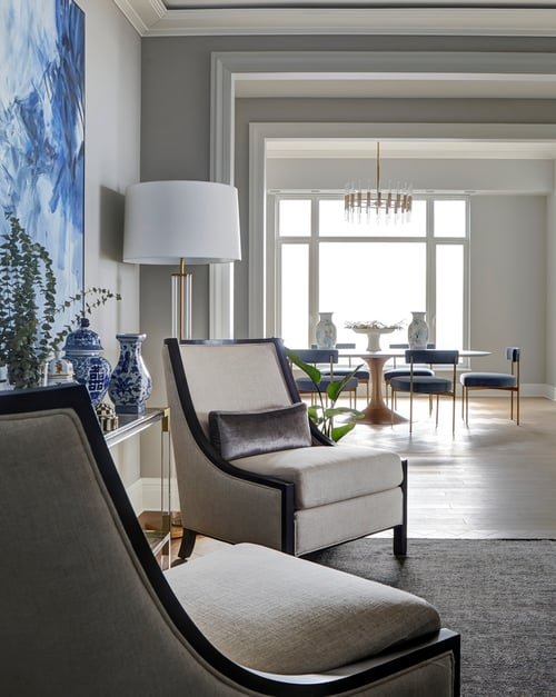 A small seating area with two dark wood and cream wing-backed chairs with a view of a petite dining room set with dark grey velvet upholstery -  living room design by Jasmin Reese Interiors, Chicago, USA.