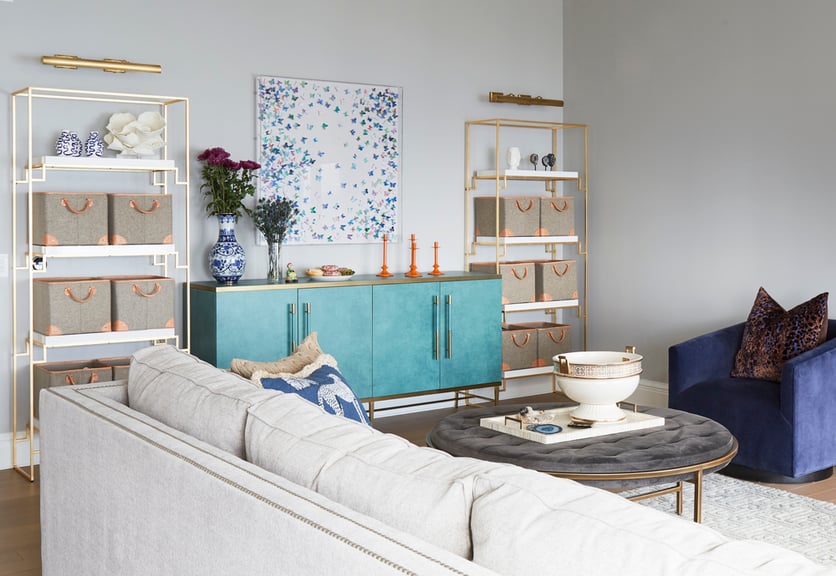 A living room designed by Jasmin Reese Interiors: whimsical butterfly art, large sofa, storage baskets on shelves. 