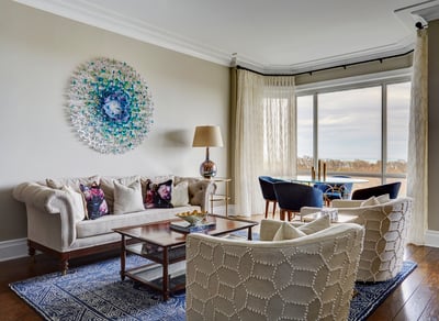 A side view of a cream and blue living room with a blue geometric area rug and blue, turquoise, and white cloth art on the focal wall - living room design by Jasmin Reese Interiors, Chicago, USA.