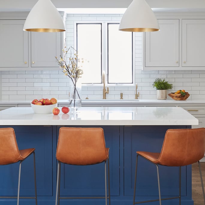 A bright blue and white kitchen with orange barstools, interior design by Jasmin Reese, Chicago. 